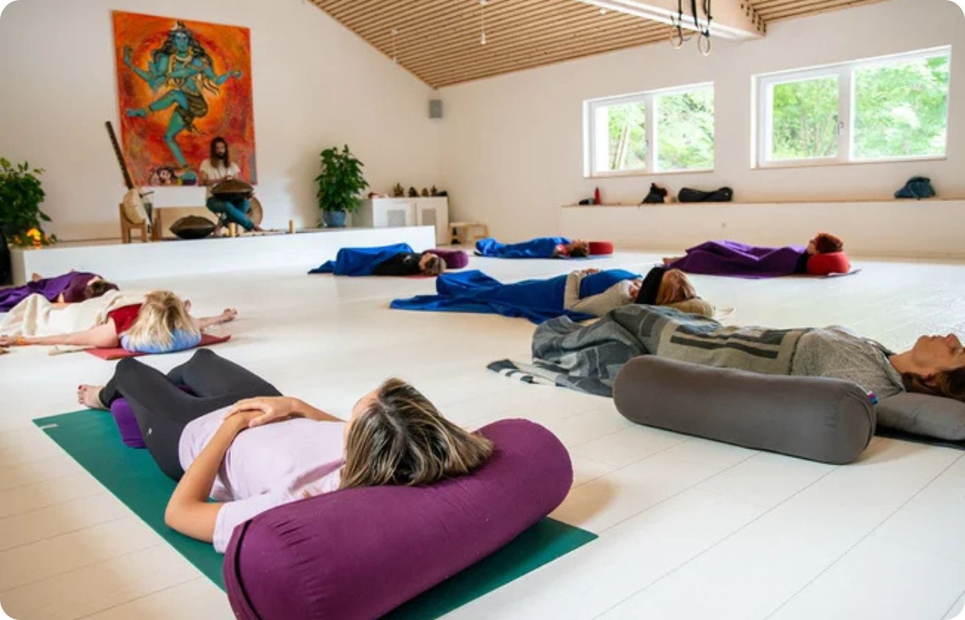 Où faire une retraite yoga en France ? 1 Sanskriti : Séance de relaxation guidée en studio de yoga, participantes allongées en savasana avec bolsters, retraite yoga en France