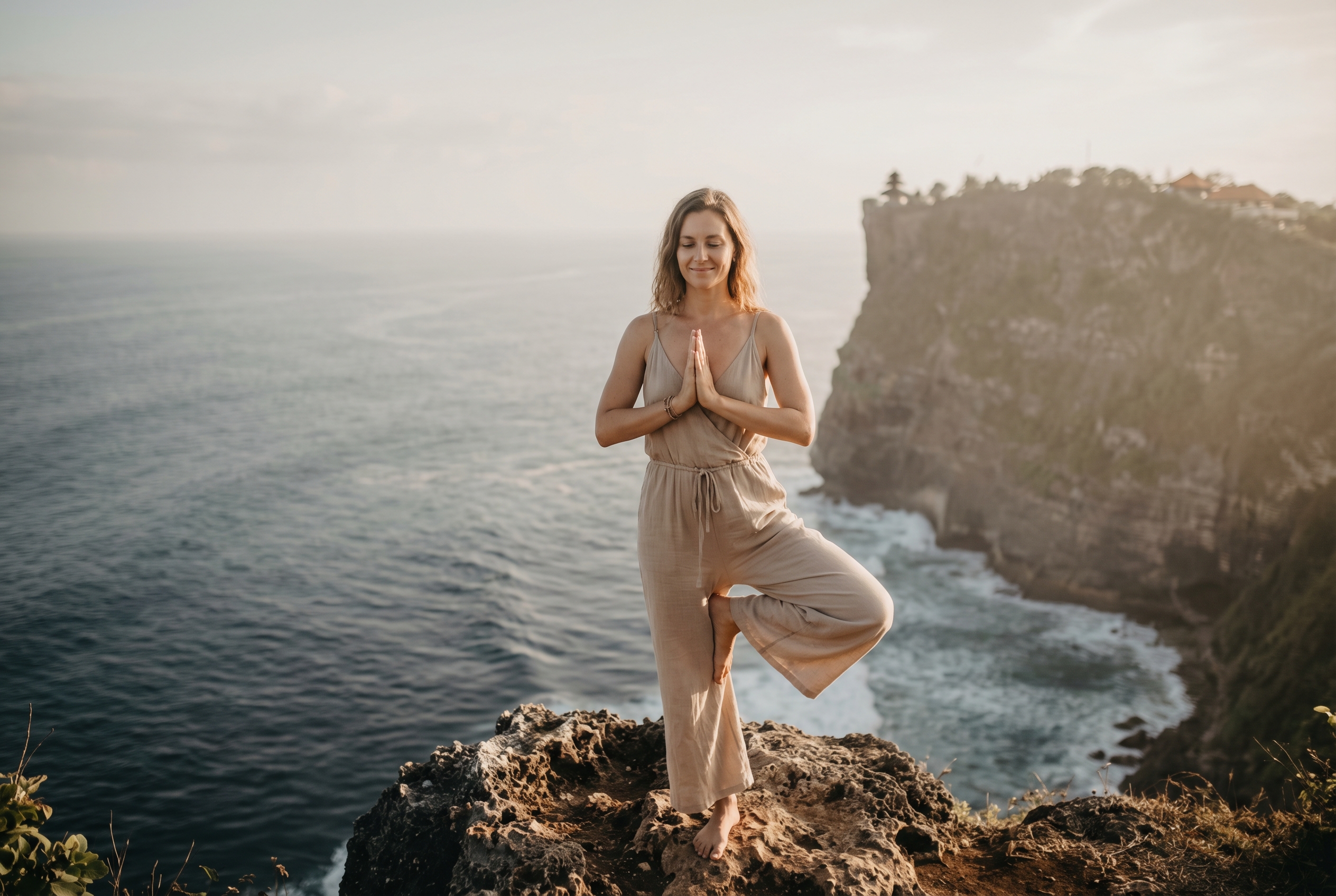 Retraite bien-être à Bali : le guide complet 1 Femme dans la position de l'arbre, les mains en prière, au bord d'une falaise à Bali.