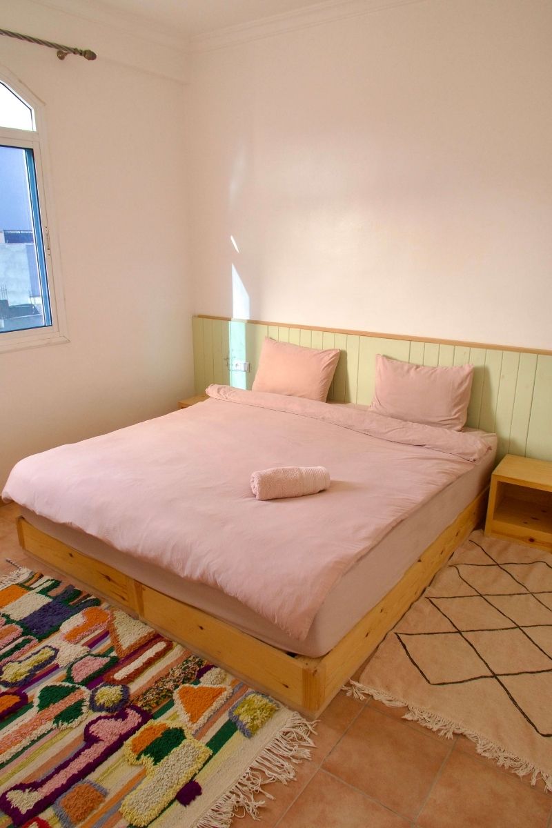 Retraite yoga & surf au Maroc : 7 jours à Tamraght avec Get Salty Guesthouse 3 Chambre double aux tons pastel avec tapis berbère coloré, dans la guesthouse de la retraite Get Salty à Tamraght, Maroc.