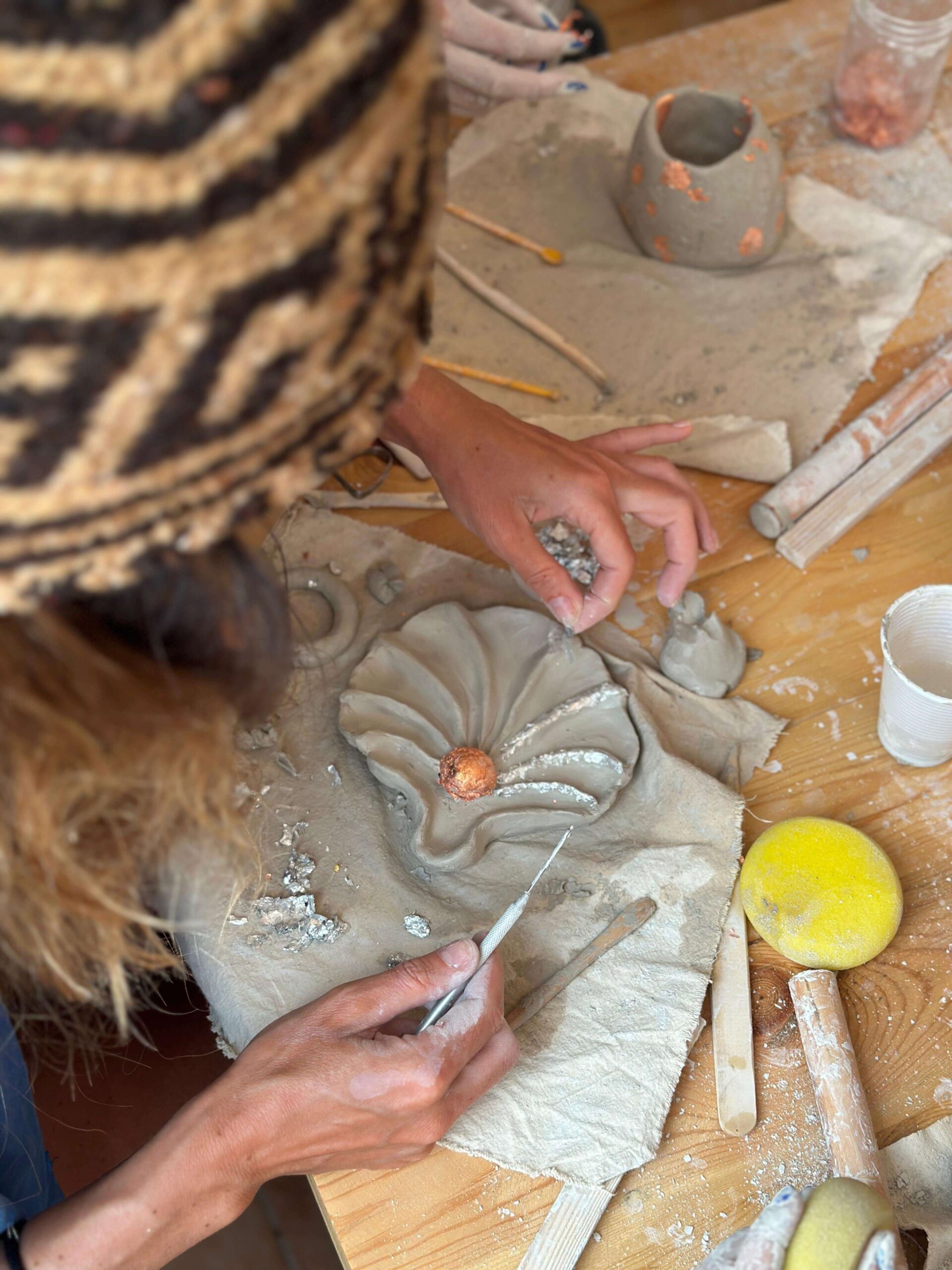 Retraite yoga & surf au Maroc : 7 jours à Tamraght avec Get Salty Guesthouse 2 Mains façonnant une pièce d'argile en forme de coquillage avec feuille dorée, lors d'un atelier poterie en retraite Get Salty Guesthouse à Tamraght.