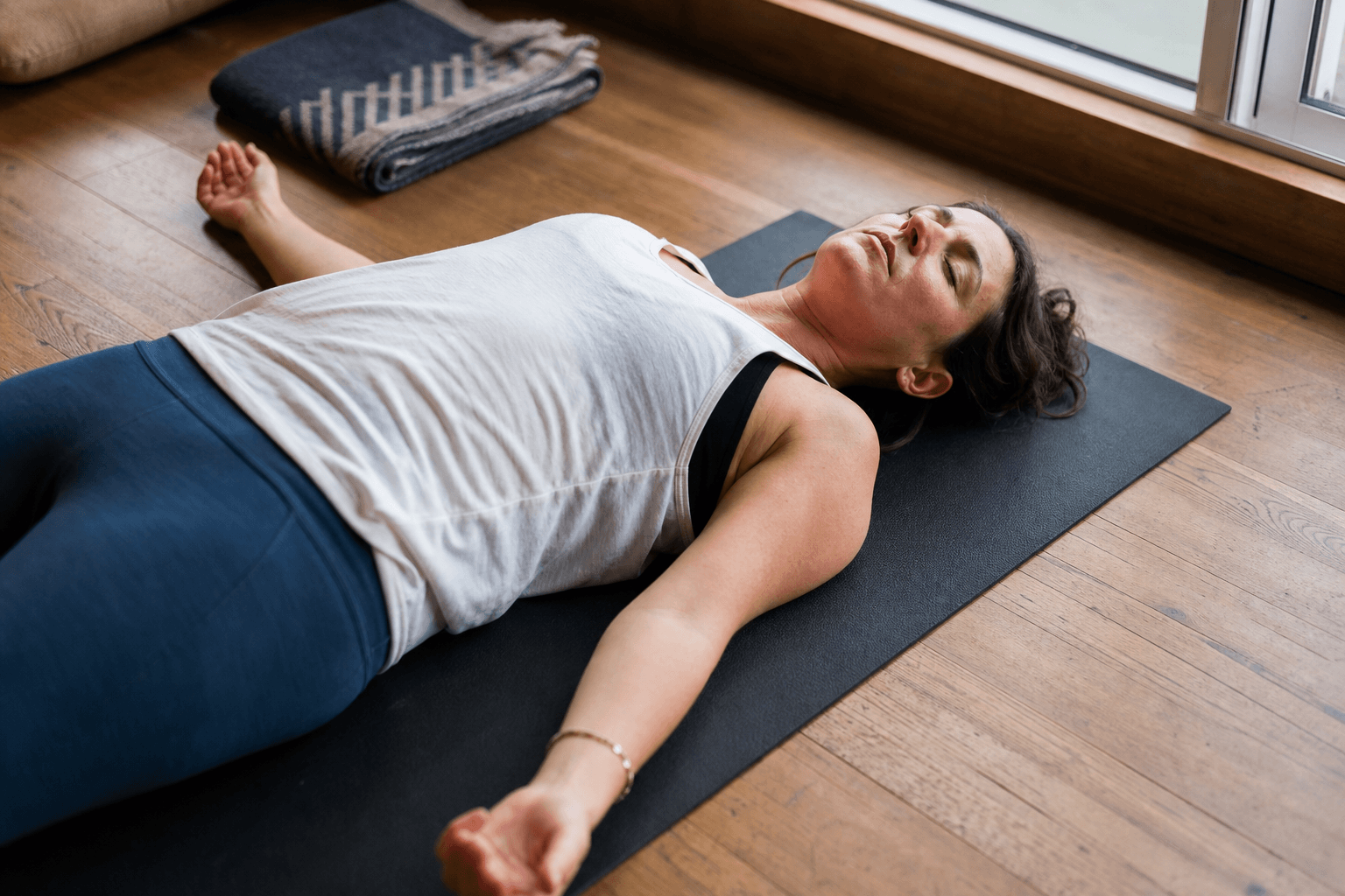 Ashtanga yoga : origines, principes et guide complet 3 Femme en Savasana après séance ashtanga, repos profond et intégration, lumière naturelle, tapis yoga bois